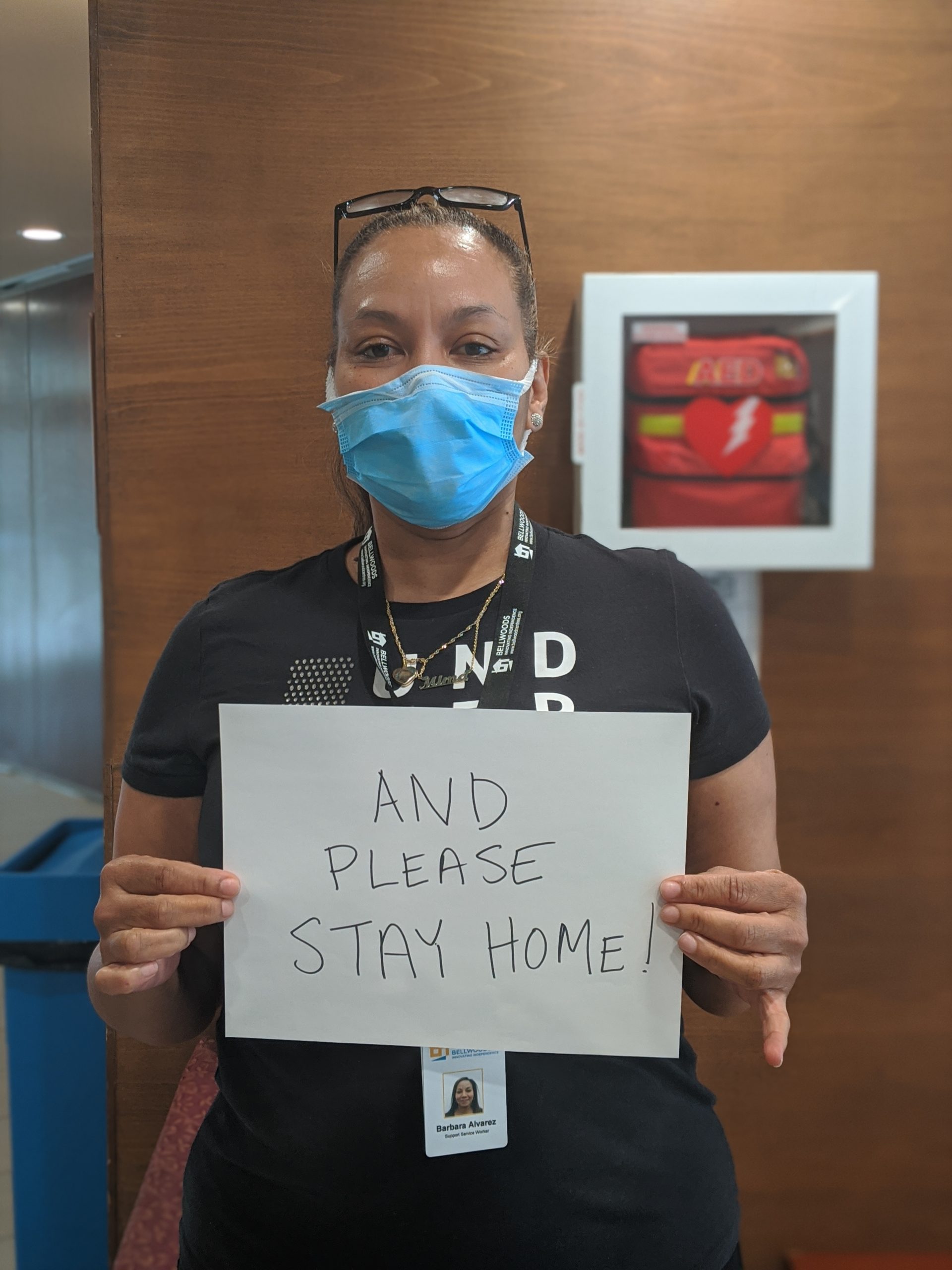 Bellwoods worker wearing a covid-19 mask, holding a sign that says "please stay home"